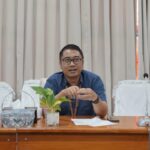 Pelaku UMKM sedang menghitung uang hasil penjualan dan mencatat transaksi di buku kas sederhana di meja usaha kecil.
