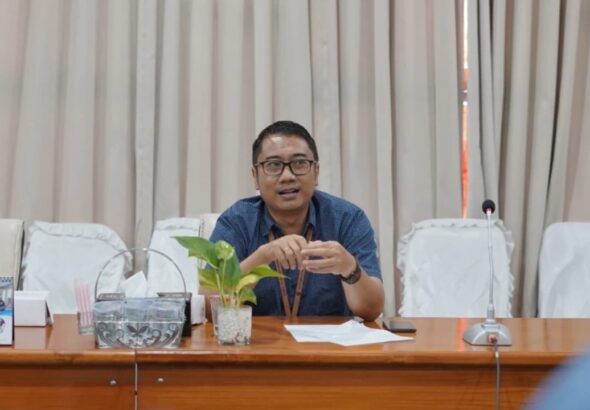 Pelaku UMKM sedang menghitung uang hasil penjualan dan mencatat transaksi di buku kas sederhana di meja usaha kecil.