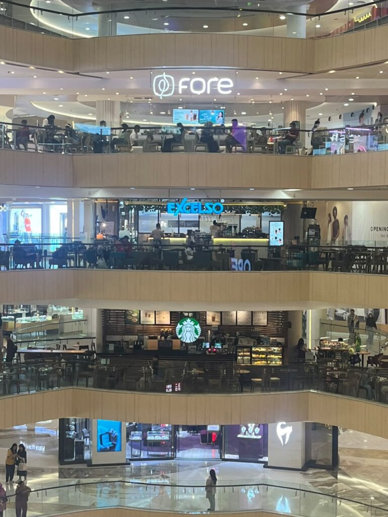 Tiga jaringan kedai kopi - Fore Coffee, Excelso, dan Starbucks - tampak berdiri secara vertikal di atrium Tunjungan Plaza, Surabaya, Minggu malam (26/7/2026)